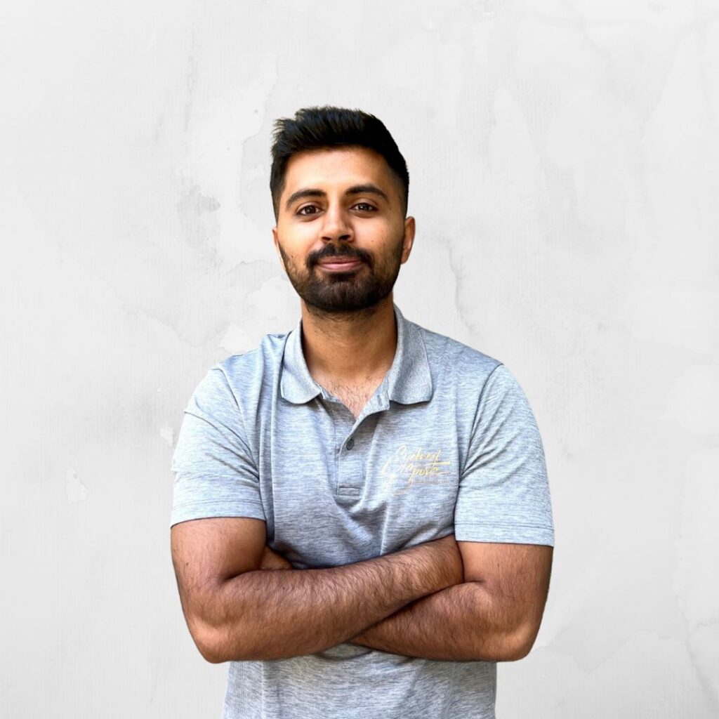A person stands confidently with arms crossed, wearing a light grey polo shirt with "Sydney Sports Massage" embroidered.