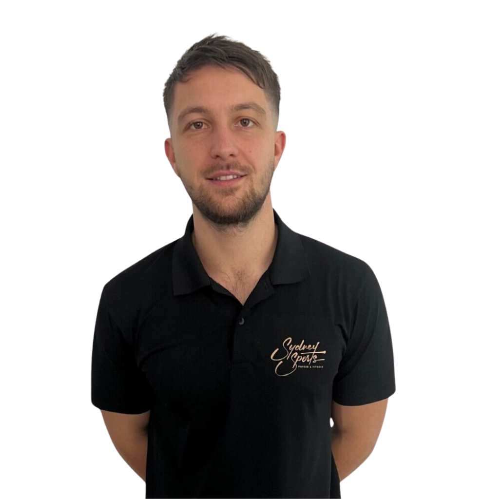 A man wearing a black polo shirt with "Sydney Sports" text stands against a plain background, hands behind his back, smiling slightly.