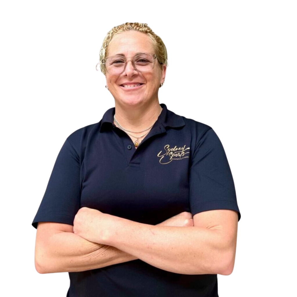 A person with short hair, smiling and crossing their arms, wears a navy polo shirt with "Sydney Sports Massage" written on it.