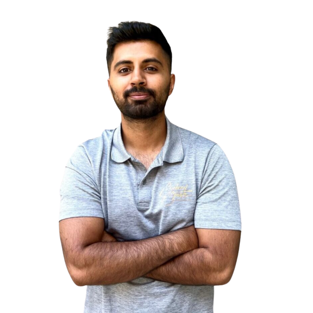 A person stands with arms crossed, wearing a light gray polo shirt with "Sydney Sports Massage" written on it, against a plain, white background.