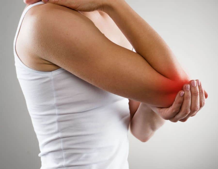 A person wearing a white tank top holds their elbow, highlighted in red, indicating pain or injury, with a neutral gray background.